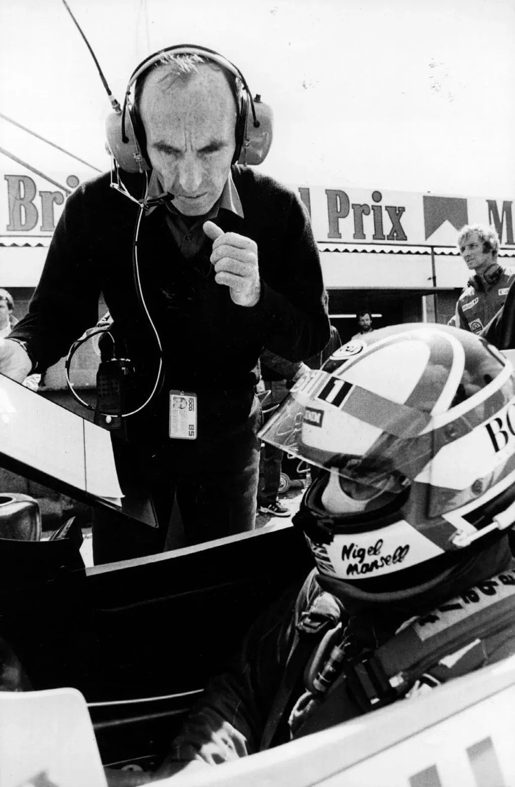Black and white photograph of Frank Williams leaning over Nigel Mansell in his cockpit at Brands Hatch in 1985.